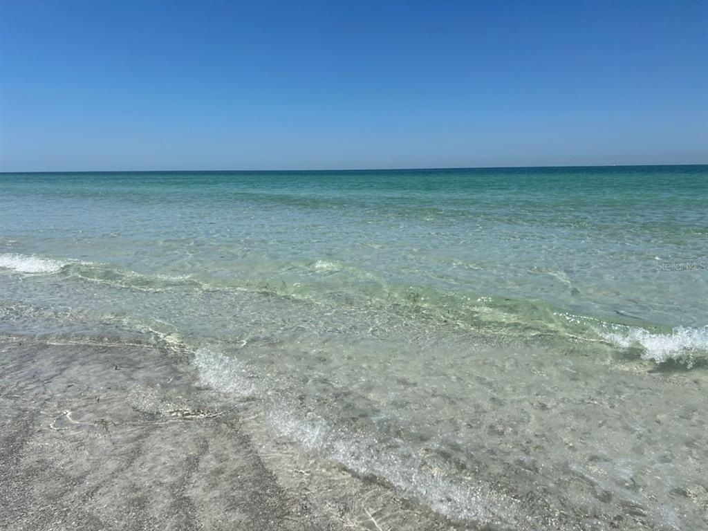 A view of clear, shallow ocean water meeting a sandy beach under a blue sky — 586 140TH AVENUE E UNIT 2, MADEIRA BEACH, FL