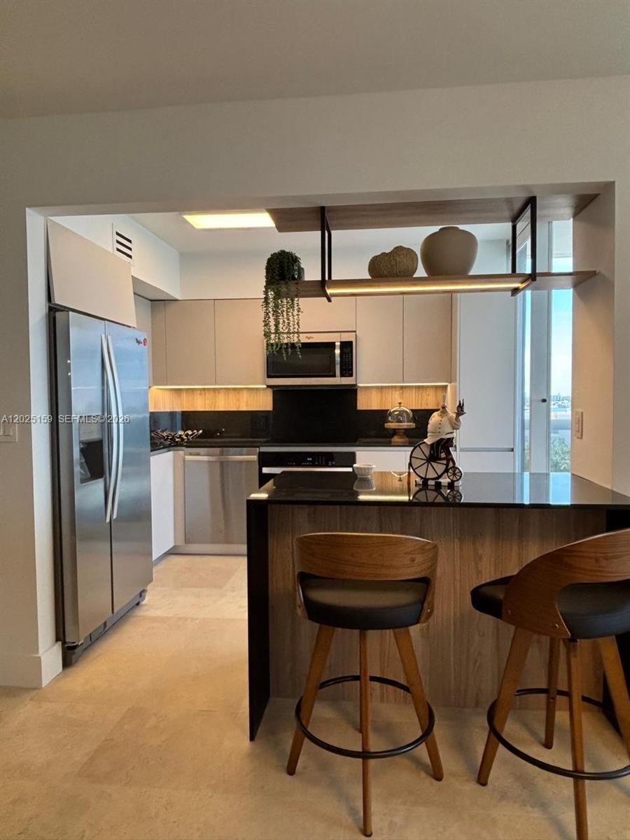 A modern kitchen features stainless steel appliances, wood-toned cabinetry, and a black-topped breakfast bar — 6301 Collins Ave # 908, Miami Beach FL 33141, MIAMI BEACH, FL