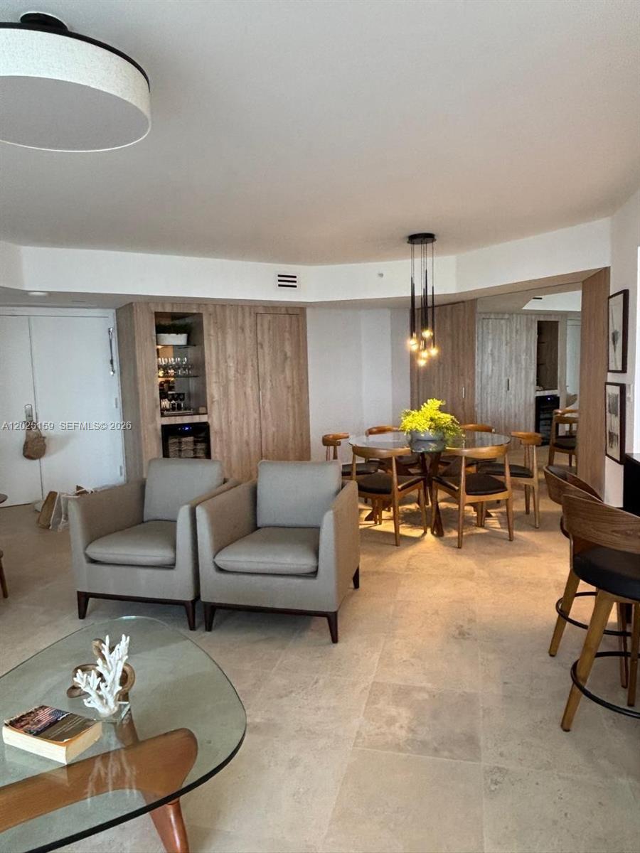 A living and dining area features light wood cabinetry, a glass table, and stone flooring — 6301 Collins Ave # 908, Miami Beach FL 33141, MIAMI BEACH, FL