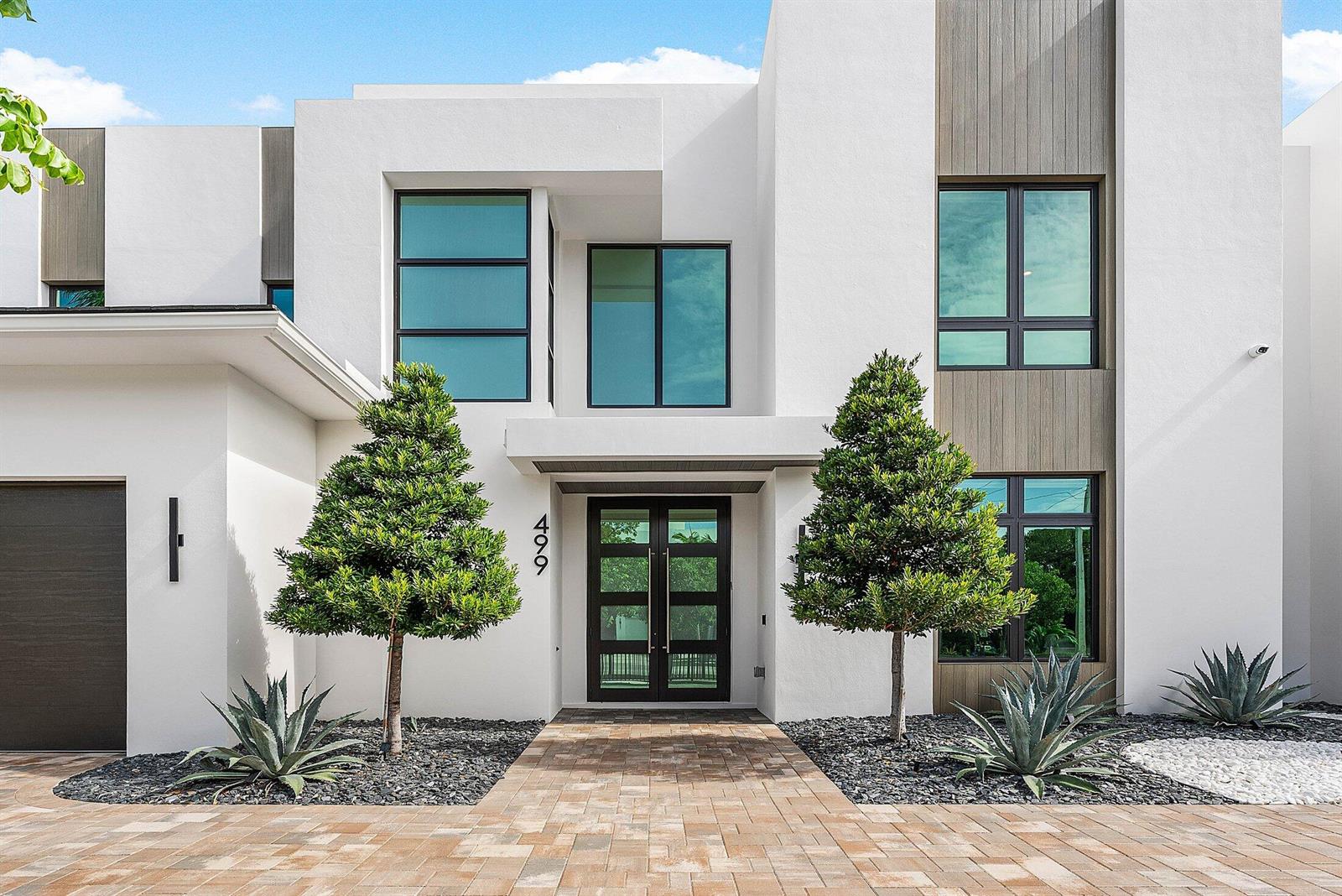 A modern two-story house features white stucco walls, wood accents, and a paved front walkway — 499 NE 4th Street, Boca Raton FL 33432, BOCA RATON, FL