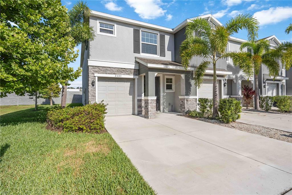 A two-story townhome with a gray stucco exterior, stone accents, and a single-car garage — 2683 MIDNIGHT PEARL DRIVE, SARASOTA, FL