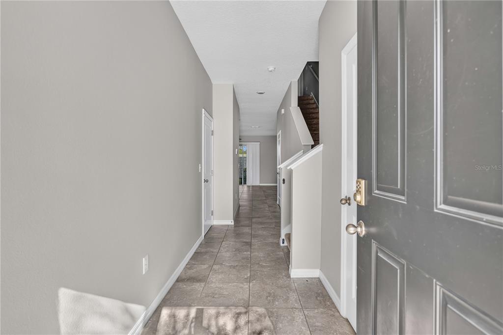 An entryway with tiled flooring leads to a hallway with a staircase and white doors — 2683 MIDNIGHT PEARL DRIVE, SARASOTA, FL