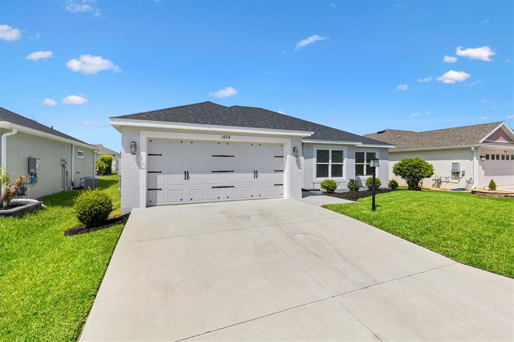 A single-story house with a white garage door, concrete driveway, and green lawn — 1574 ROWELL STREET, THE VILLAGES, FL