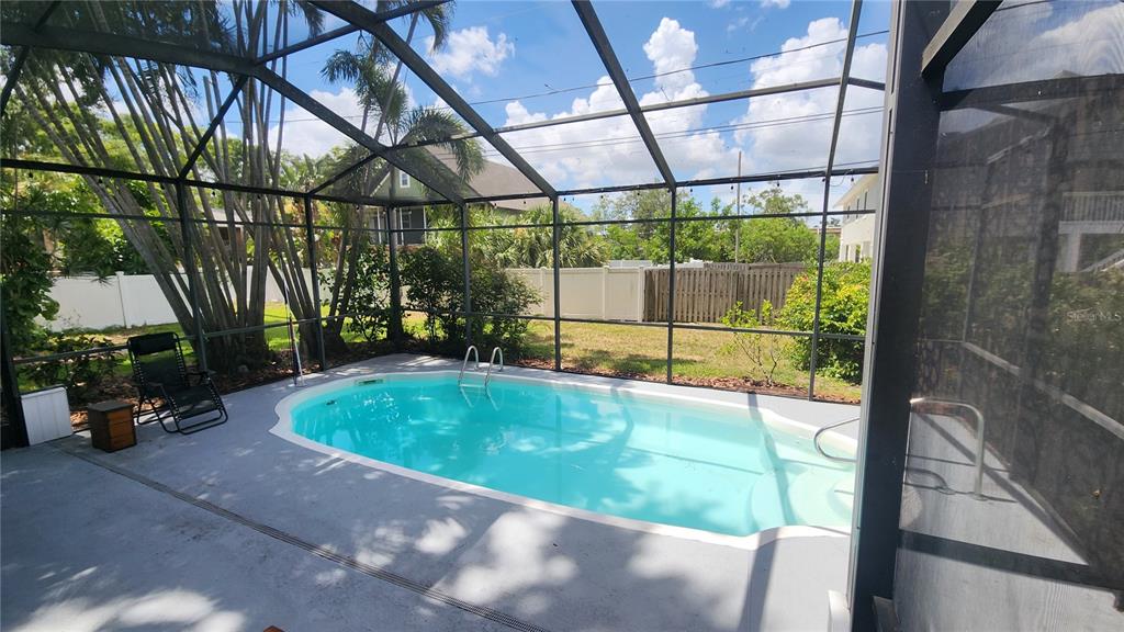 A screened-in patio features a swimming pool with a ladder and surrounding palm trees — 155 69TH AVENUE N, ST PETERSBURG, FL