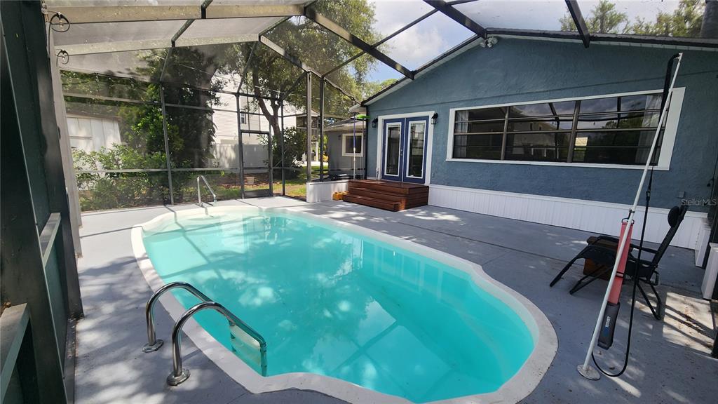 A screened-in patio features a swimming pool, concrete deck, and a blue house exterior — 155 69TH AVENUE N, ST PETERSBURG, FL