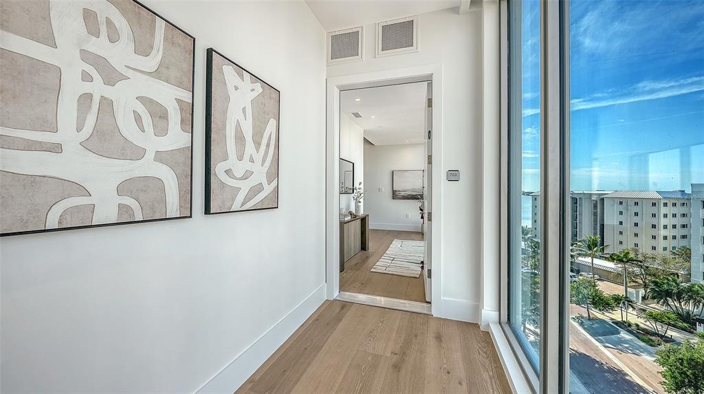 A hallway with light wood floors leads to an interior room, featuring abstract wall art — 253 GOLDEN GATE POINT UNIT 703, SARASOTA, FL