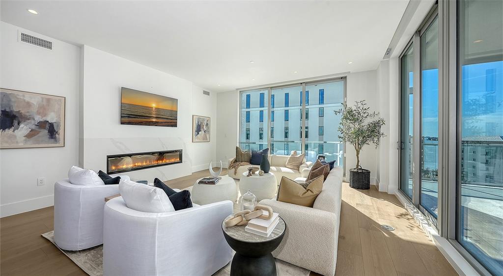 A modern living room features a linear fireplace, white furniture, and floor-to-ceiling windows — 253 GOLDEN GATE POINT UNIT 703, SARASOTA, FL