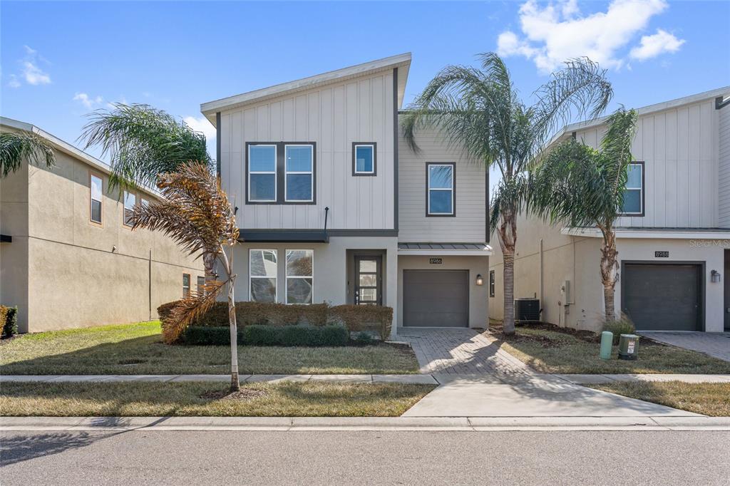 A two-story modern house with a gray garage and light-colored siding stands under a blue sky — 8986 CABOT CLIFFS DRIVE, DAVENPORT, FL