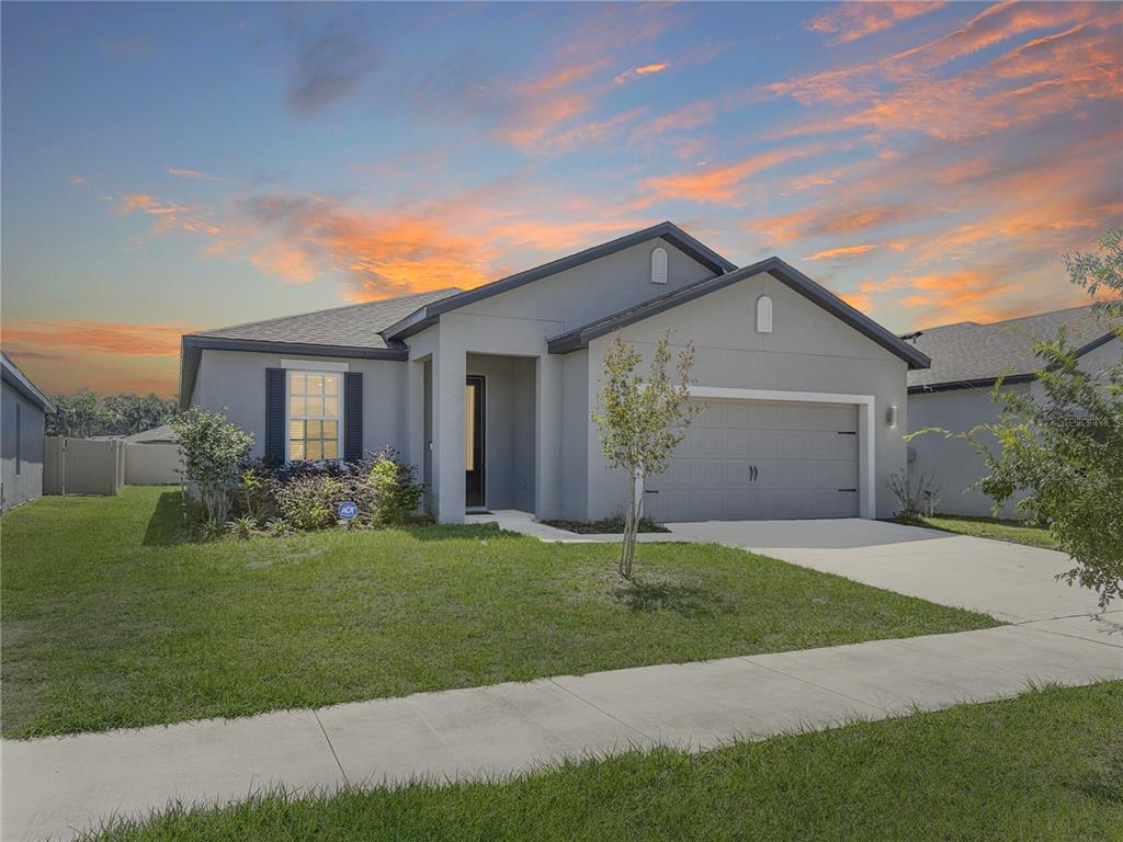 A single-story gray house with a two-car garage and a front lawn at sunset — 6022 DOLOSTONE DRIVE, LAKELAND, FL