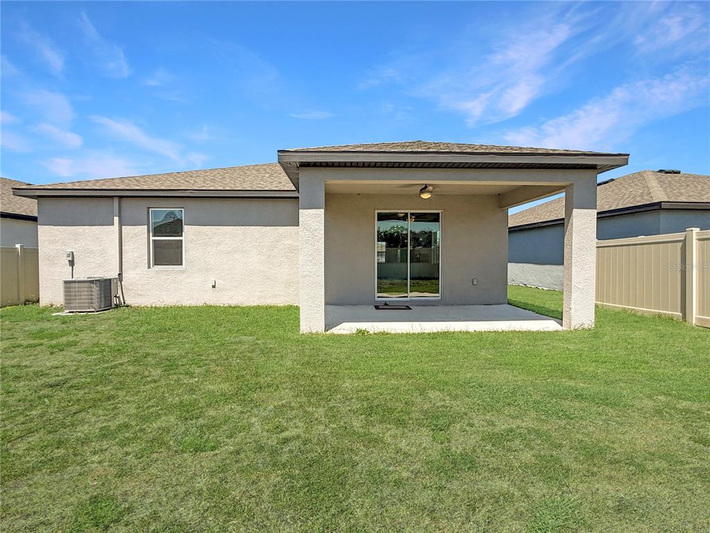 The back exterior of a house features a covered concrete patio and a grassy yard — 6022 DOLOSTONE DRIVE, LAKELAND, FL