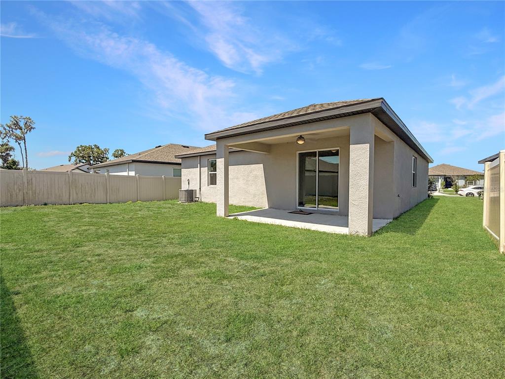 A beige house with a covered concrete patio and a fenced backyard under a blue sky — 6022 DOLOSTONE DRIVE, LAKELAND, FL