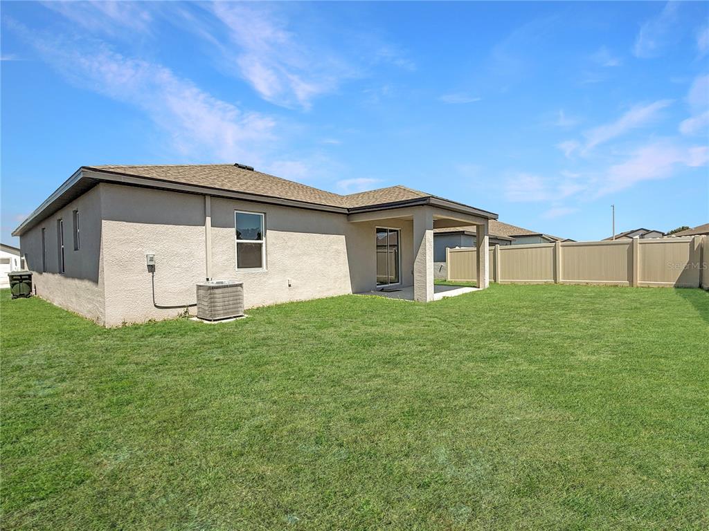 The exterior view shows the back of a house with a covered patio and lawn — 6022 DOLOSTONE DRIVE, LAKELAND, FL