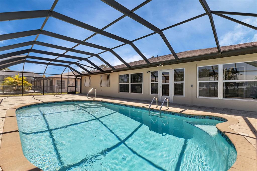 A swimming pool with a metal screen enclosure sits on a paved patio behind a house — 745 COLUMBIA STREET, PORT CHARLOTTE, FL