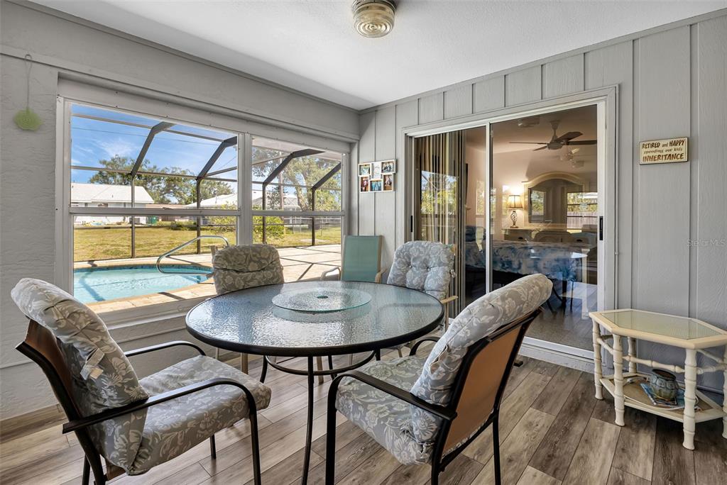 A sunroom with a glass dining table, patterned chairs, wood-look flooring, and a pool view — 745 COLUMBIA STREET, PORT CHARLOTTE, FL