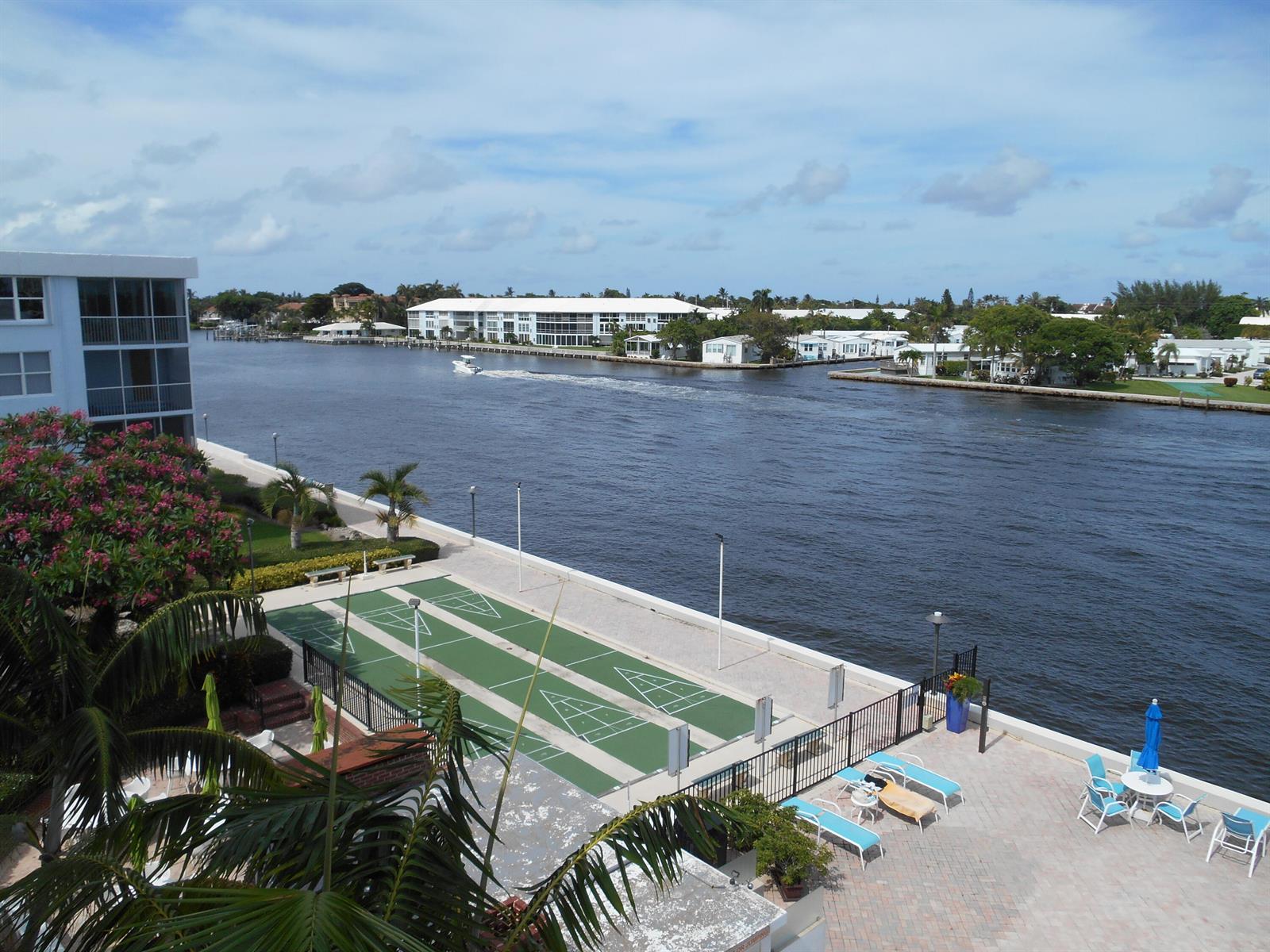 An elevated view of a waterfront shuffleboard court, patio, and canal with a passing boat — 2016 S Federal Highway # 204, Boynton Beach FL 33435, BOYNTON BEACH, FL