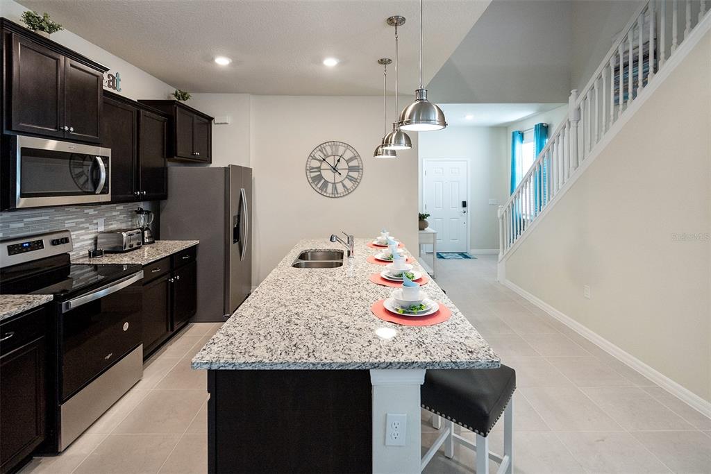 A kitchen features dark cabinets, granite countertops, a central island, and a staircase nearby — 4051 LANA AVENUE, DAVENPORT, FL