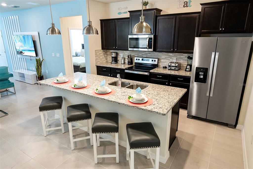 A kitchen features dark cabinetry, granite countertops, a central island with four stools, and stainless appliances — 4051 LANA AVENUE, DAVENPORT, FL