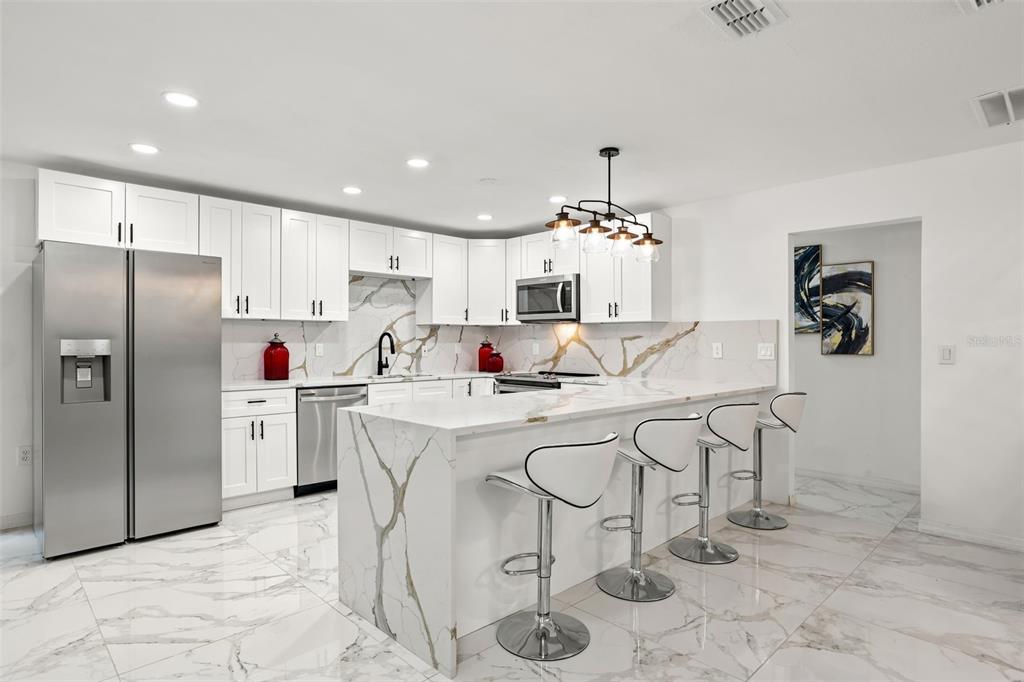 A modern kitchen features white cabinets, marble-patterned countertops, a waterfall island, and stainless steel appliances — 2629 TELSTAR AVENUE, ORLANDO, FL