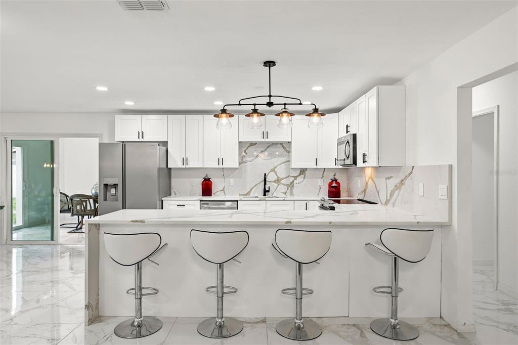 A modern kitchen features white cabinets, a marble-patterned backsplash, and a breakfast bar with stools — 2629 TELSTAR AVENUE, ORLANDO, FL