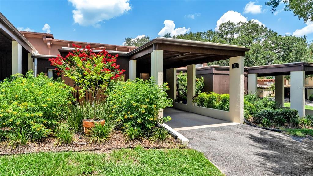 A covered walkway leads to the entrance of a building with a red-flowering shrub — 11 EL RECODO UNIT 11, LAKELAND, FL