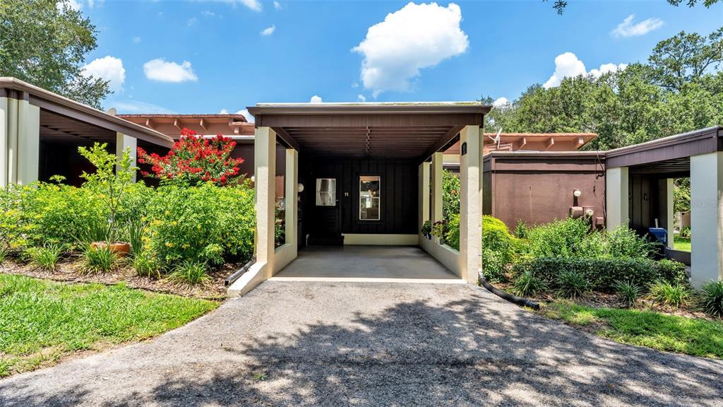 A brown house exterior features a covered carport entrance and lush green landscaping — 11 EL RECODO UNIT 11, LAKELAND, FL