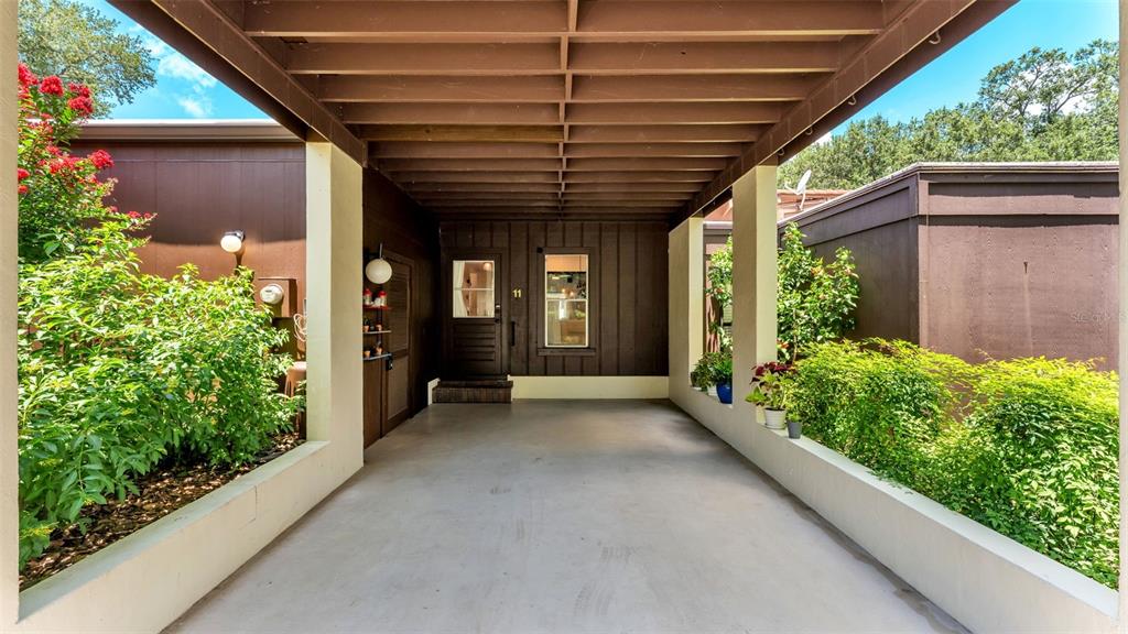A covered carport with a concrete floor leads to a dark wood exterior entrance — 11 EL RECODO UNIT 11, LAKELAND, FL