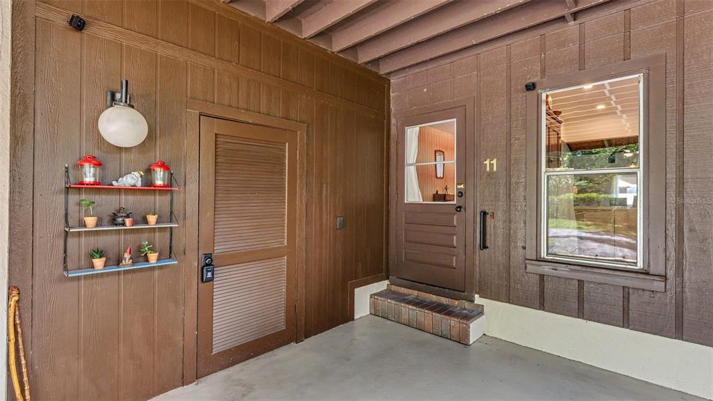 An exterior view of a brown wooden building entrance with a door, window, and shelving — 11 EL RECODO UNIT 11, LAKELAND, FL