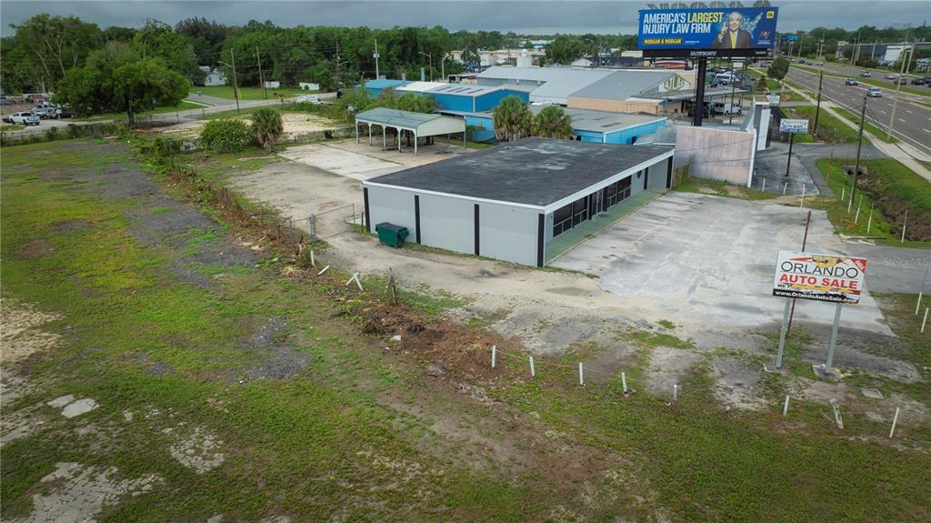 An aerial view shows a commercial building with a parking lot and adjacent vacant land — 6464 E COLONIAL DRIVE, ORLANDO, FL