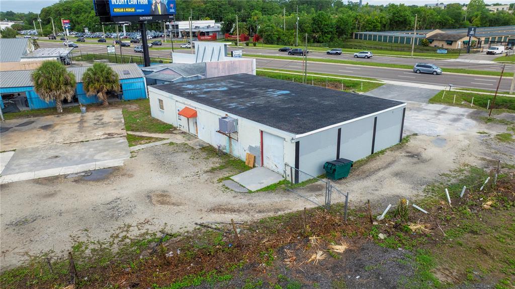 An aerial view shows a flat-roofed commercial building with a gravel lot and surrounding roads — 6464 E COLONIAL DRIVE, ORLANDO, FL