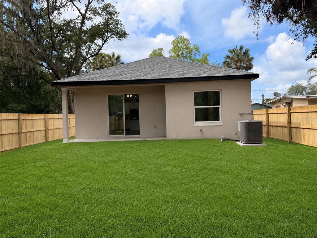 The back exterior of a tan house with a sliding glass door and a fenced yard — 1816 W 16TH STREET, SANFORD, FL