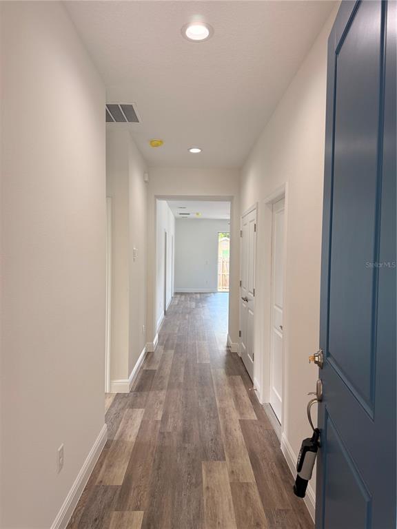 A hallway with light-colored walls and wood-look flooring leads toward an open doorway — 1816 W 16TH STREET, SANFORD, FL