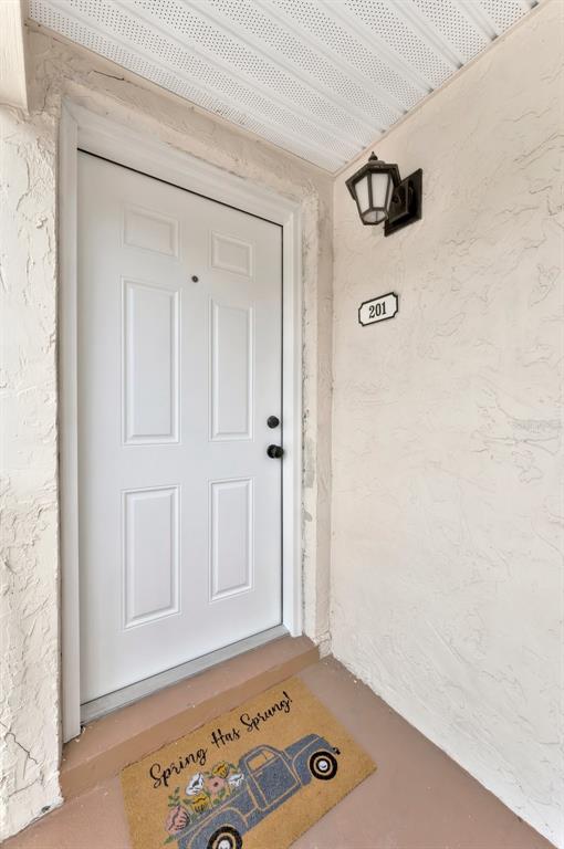 A white front door with a welcome mat and a wall-mounted light fixture — 592 100TH AVENUE N UNIT 201, ST PETERSBURG, FL
