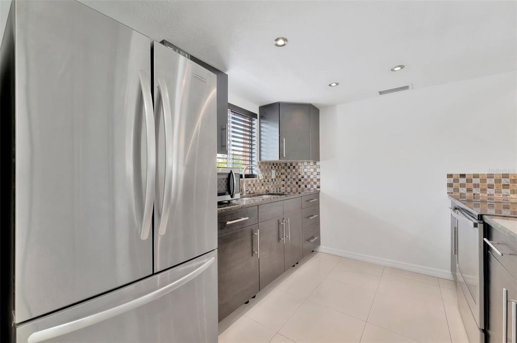 A modern kitchen features stainless steel appliances, dark wood cabinetry, and a tiled backsplash — 592 100TH AVENUE N UNIT 201, ST PETERSBURG, FL