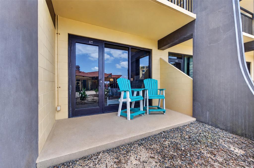 A ground-level patio features two bright blue chairs in front of a glass sliding door — 2301 S ATLANTIC AVENUE UNIT 127, DAYTONA BEACH, FL