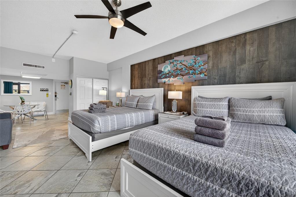 A bedroom features two beds, a wood-paneled accent wall, and an adjacent dining area — 2301 S ATLANTIC AVENUE UNIT 127, DAYTONA BEACH, FL