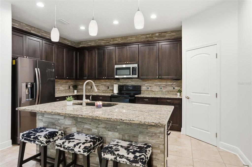 A kitchen features dark wood cabinets, granite countertops, a stone-tiled island, and three cow-print stools — 12417 CORALBEAN COURT, NEW PORT RICHEY, FL