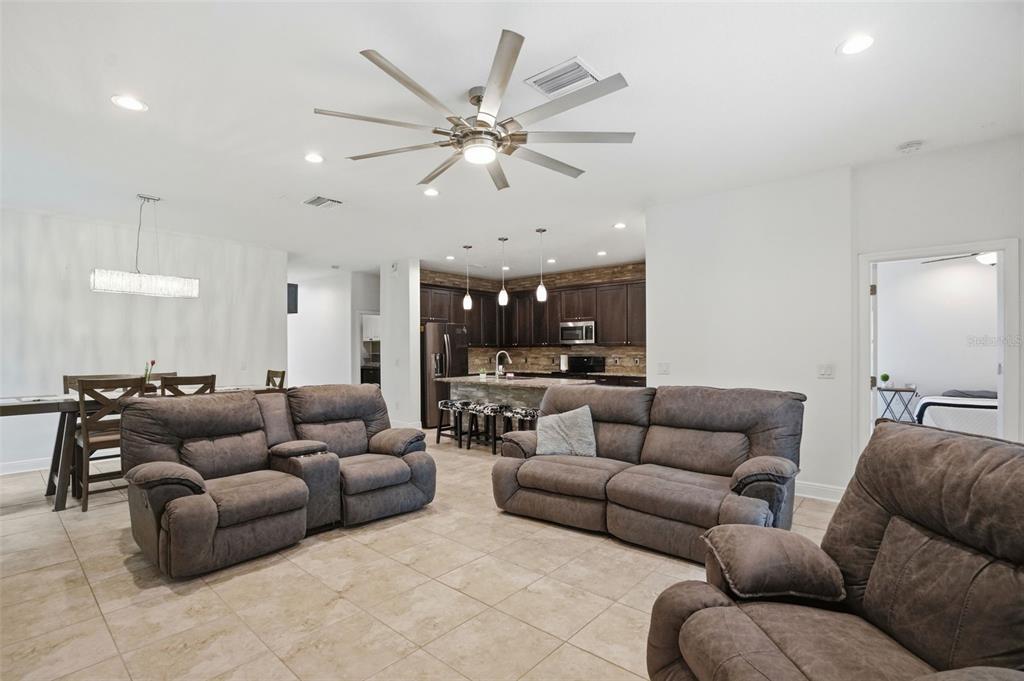 An open-concept living room features tile flooring, brown reclining sofas, and a kitchen with dark cabinets — 12417 CORALBEAN COURT, NEW PORT RICHEY, FL