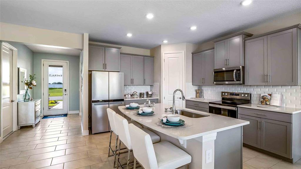 A modern kitchen features white cabinetry, a central island, stainless steel appliances, and wood flooring — 4306 SILVER BIRCH COURT, PALMETTO, FL