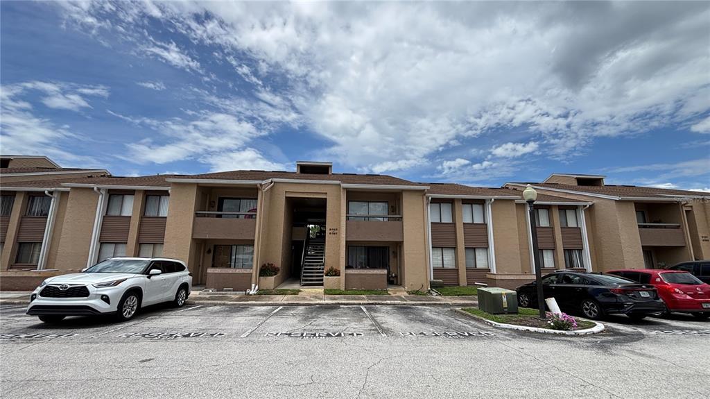 A multi-story apartment building with tan stucco walls and a parking lot in front — 5169 VINELAND ROAD UNIT B208, ORLANDO, FL