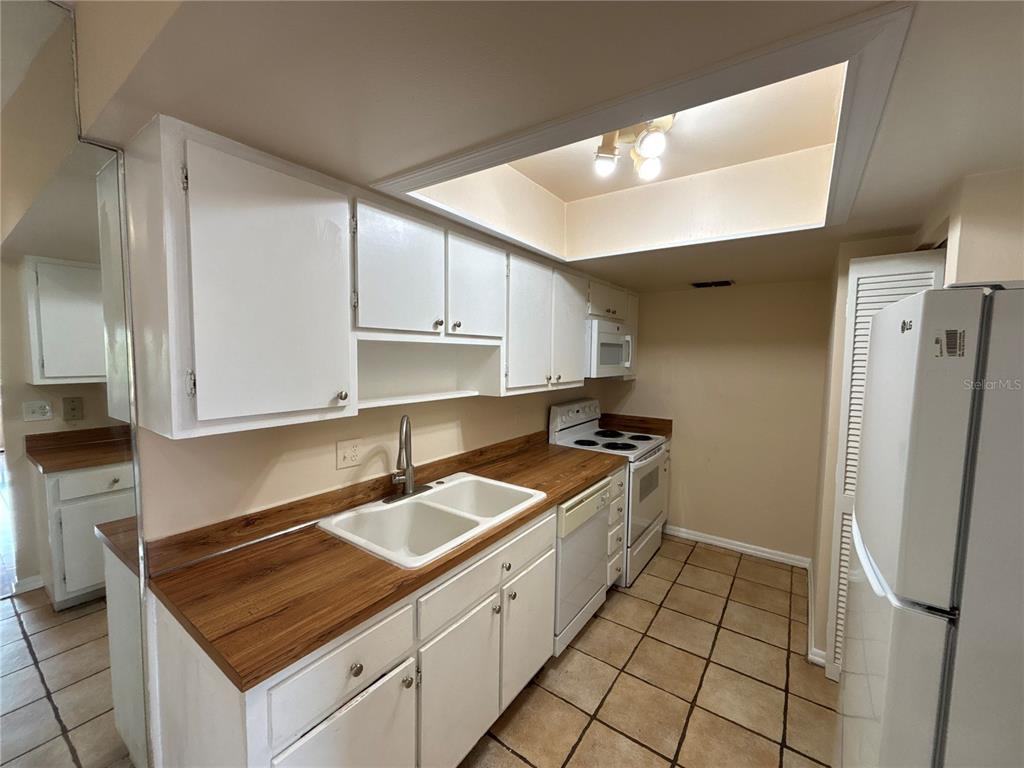 A kitchen features white cabinets, wood-look countertops, a double sink, and tiled flooring — 5169 VINELAND ROAD UNIT B208, ORLANDO, FL