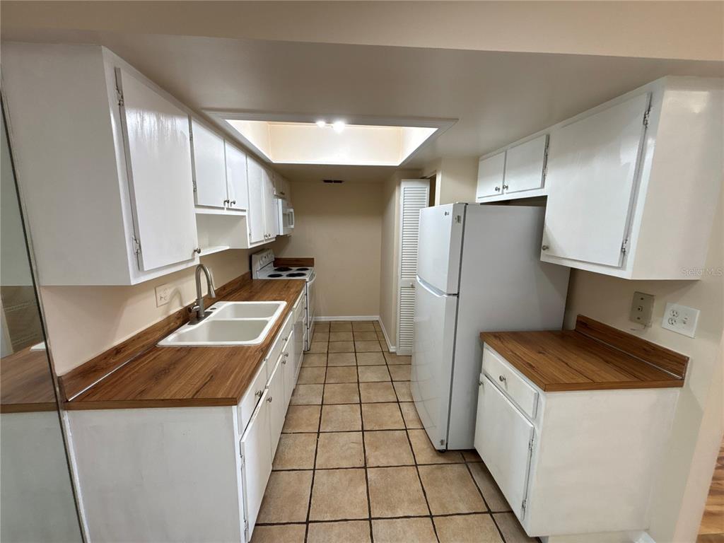 A galley kitchen features white cabinets, wood-look countertops, a white refrigerator, and tiled flooring — 5169 VINELAND ROAD UNIT B208, ORLANDO, FL