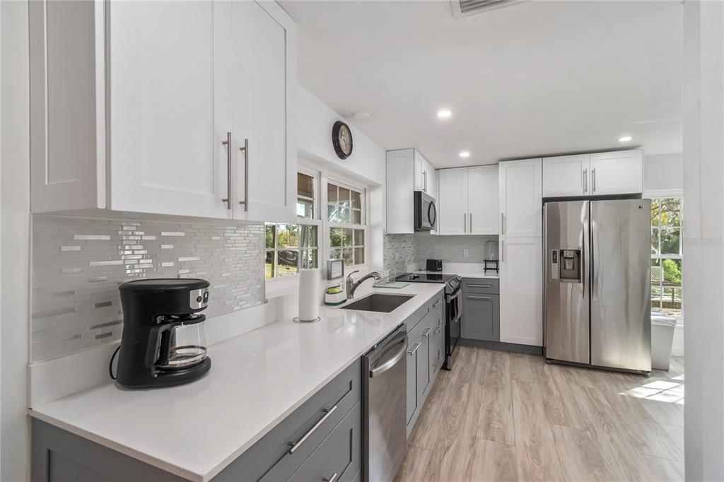 A kitchen features white upper cabinets, gray lower cabinets, white countertops, and stainless steel appliances — 510 SE 19TH STREET, OCALA, FL