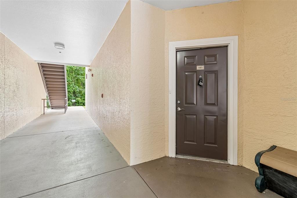 A brown apartment door numbered 105 is located in an outdoor hallway with concrete floors — 5125 PALM SPRINGS BOULEVARD UNIT 15105, TAMPA, FL