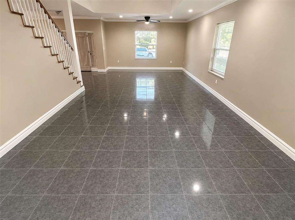A spacious room features gray tiled flooring, a staircase with white railings, and neutral walls — 3522 W PRICE AVENUE, TAMPA, FL