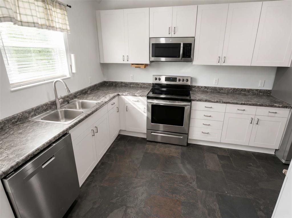 A kitchen features white cabinets, stainless steel appliances, dark countertops, and slate-style tile flooring — 3522 W PRICE AVENUE, TAMPA, FL