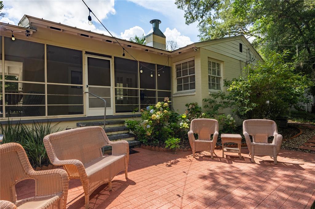 A brick patio features wicker furniture in front of a house with a screened porch — 434 NW 25TH STREET, GAINESVILLE, FL