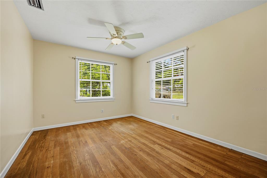 An empty bedroom features light-colored walls, hardwood floors, two windows, and a ceiling fan — 434 NW 25TH STREET, GAINESVILLE, FL