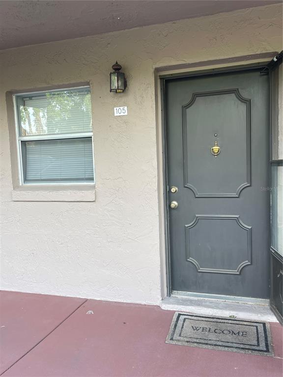 A gray front door with a brass knocker and a window on a beige wall — 150 EL DORADO UNIT 105, WINTER HAVEN, FL
