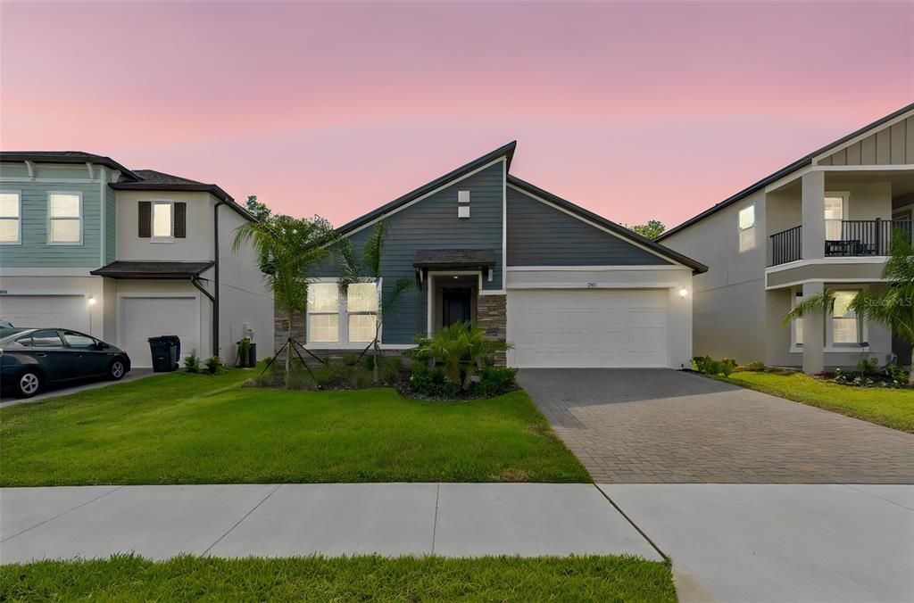 A modern single-story house with a gray siding facade, stone accents, and a paved driveway — 18542 SERENE LAKE LOOP, LUTZ, FL