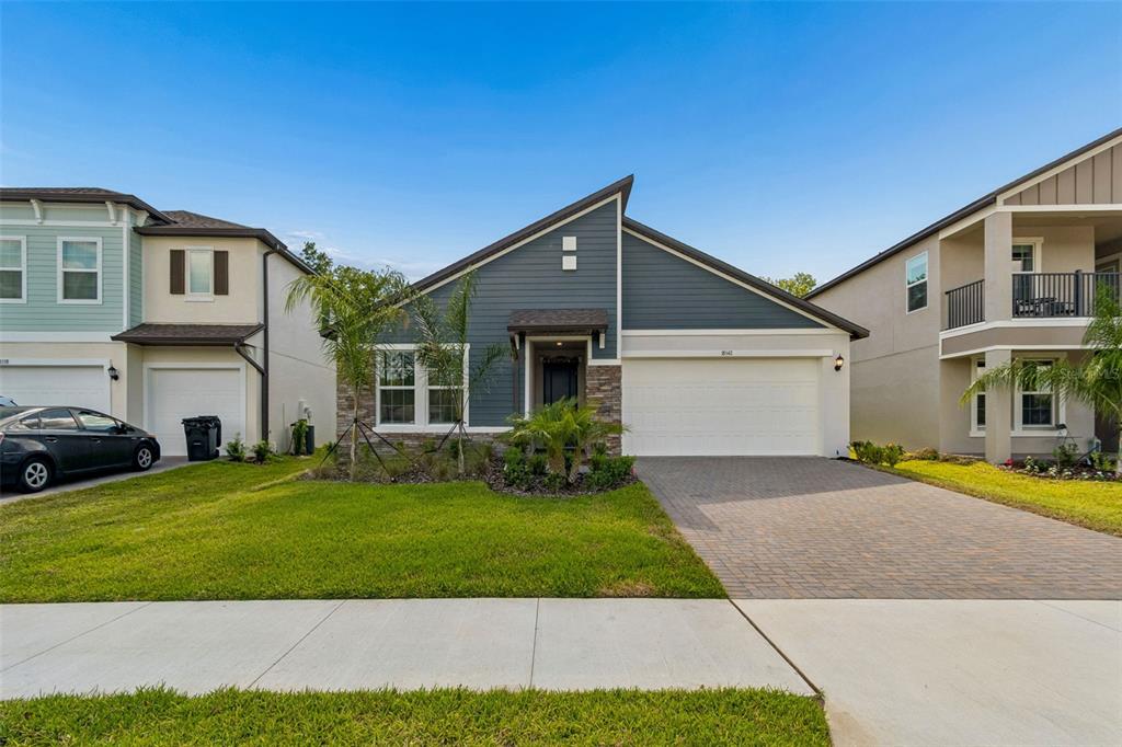 A single-story house with a blue-gray siding facade, stone accents, and a paved driveway — 18542 SERENE LAKE LOOP, LUTZ, FL